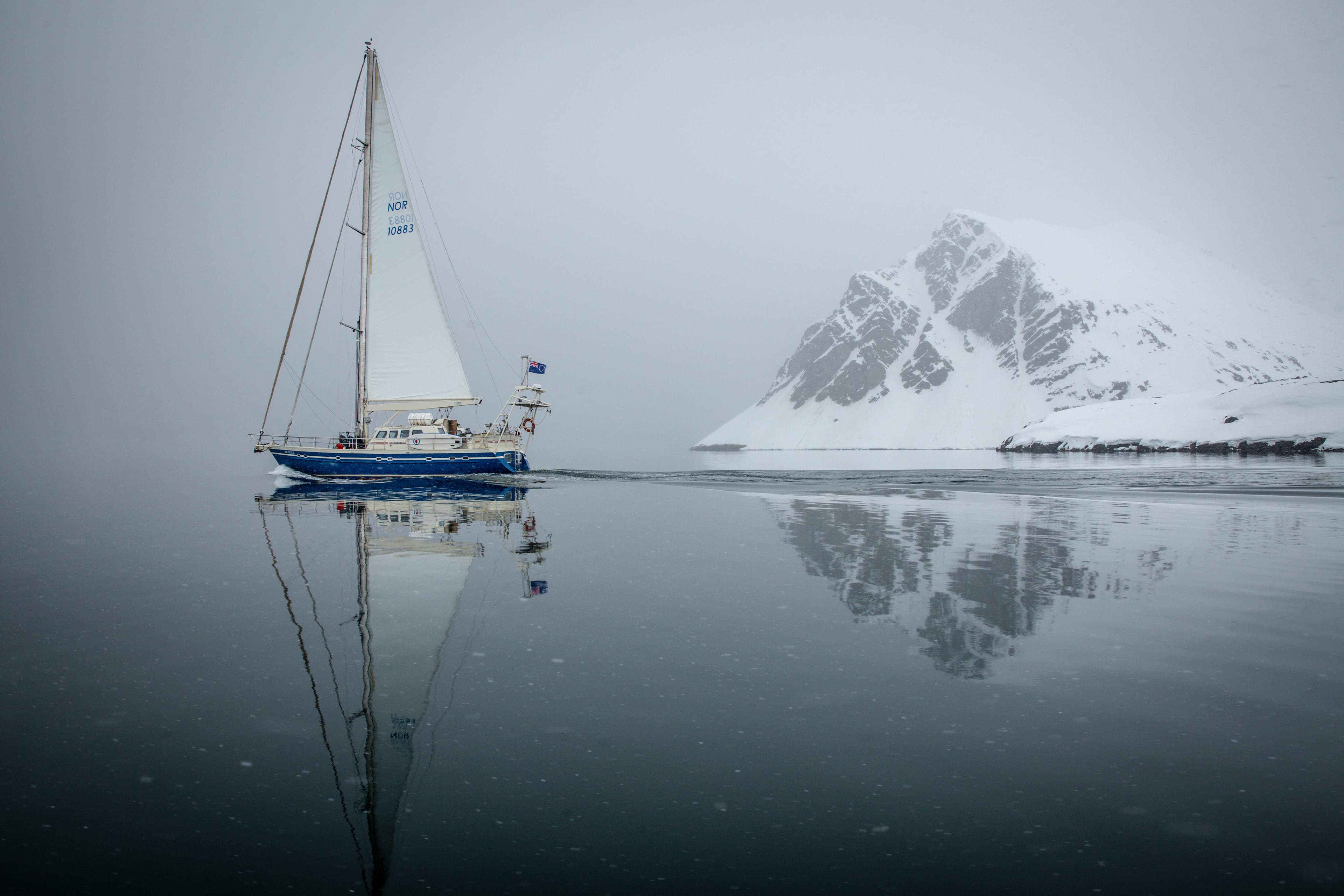 Sailboat in misty Antarctic bay with mountain reflection