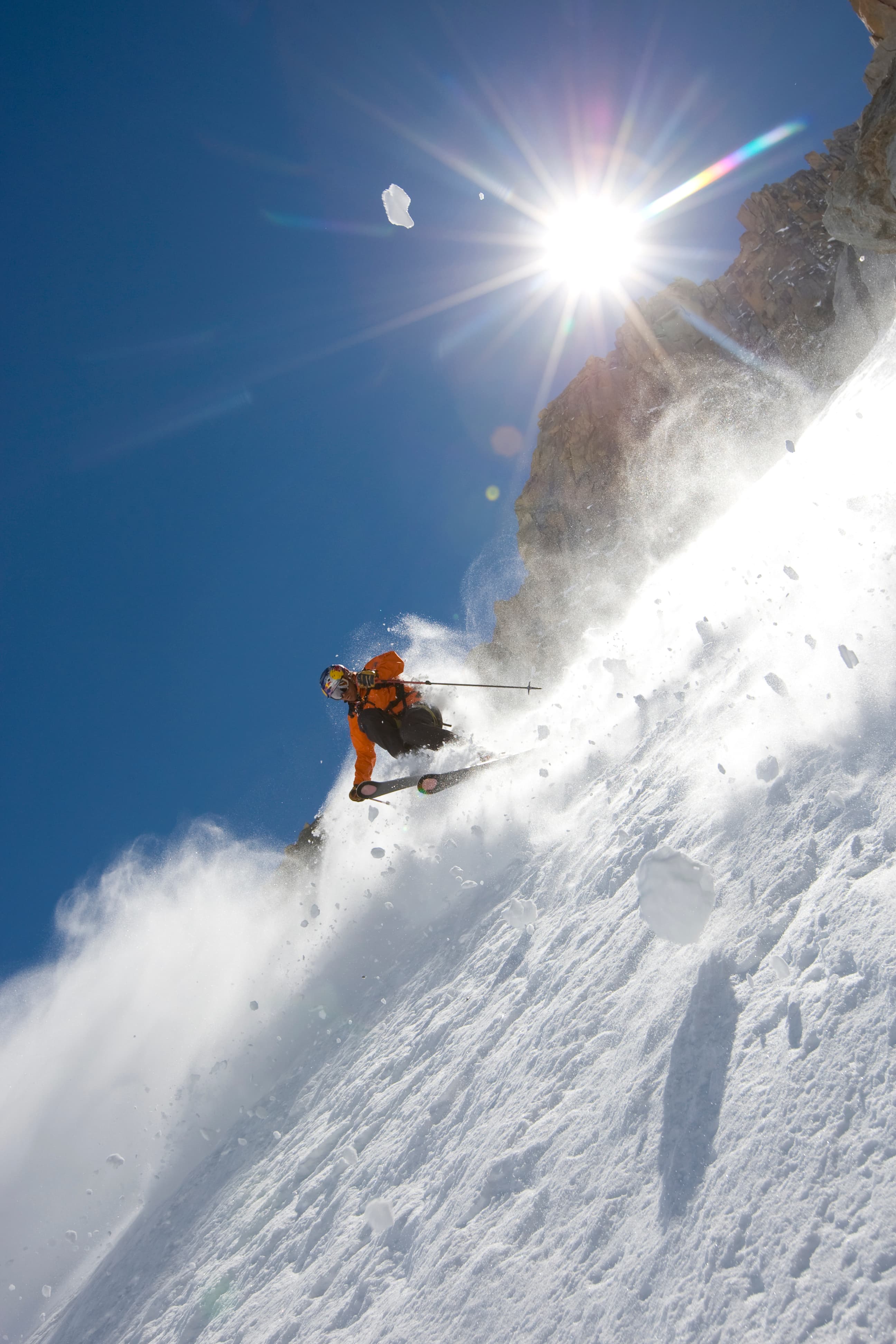 Chris Davenport charging powder in orange jacket under a star-burst sun