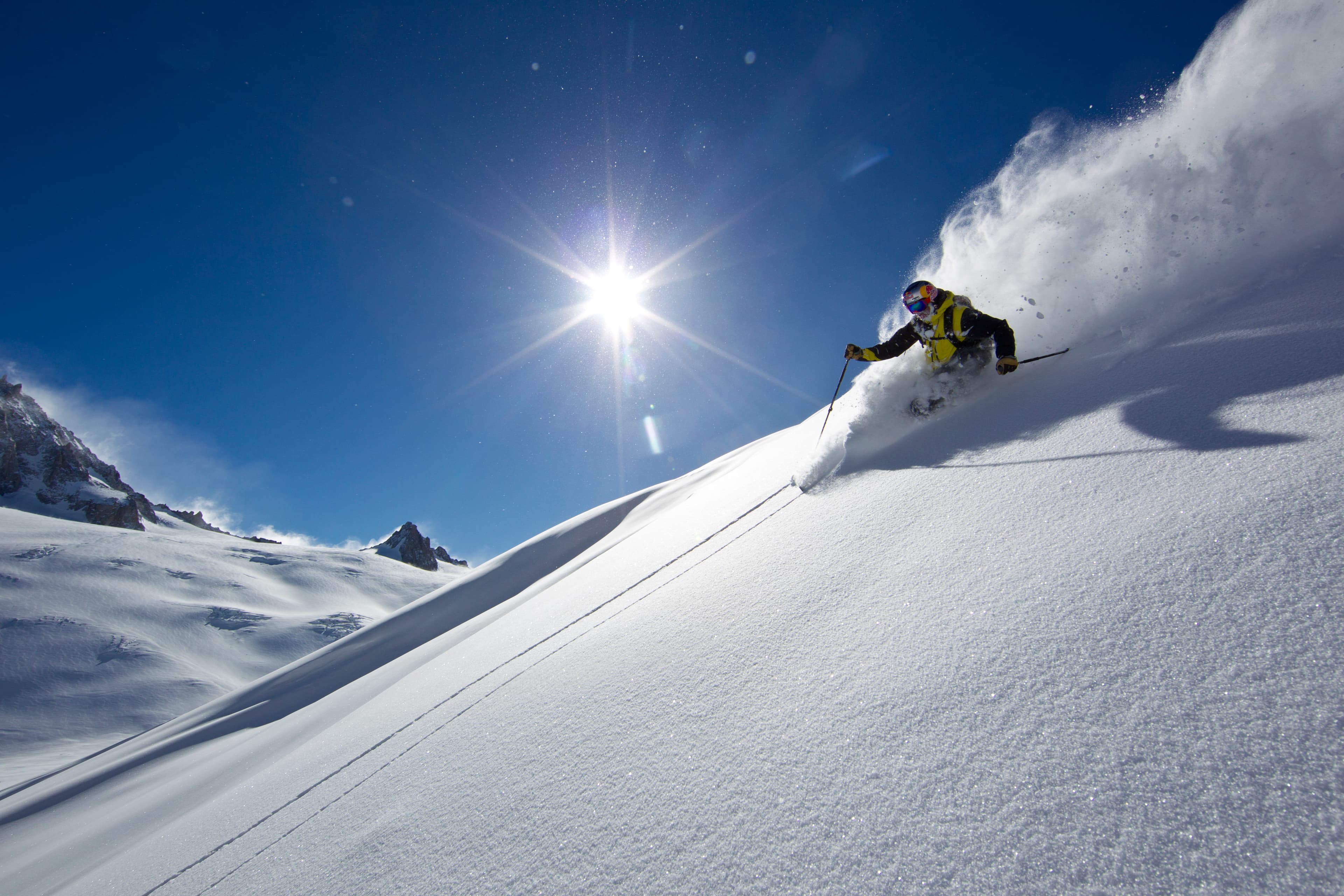 Chris Davenport in yellow jacket skiing powder against the sun