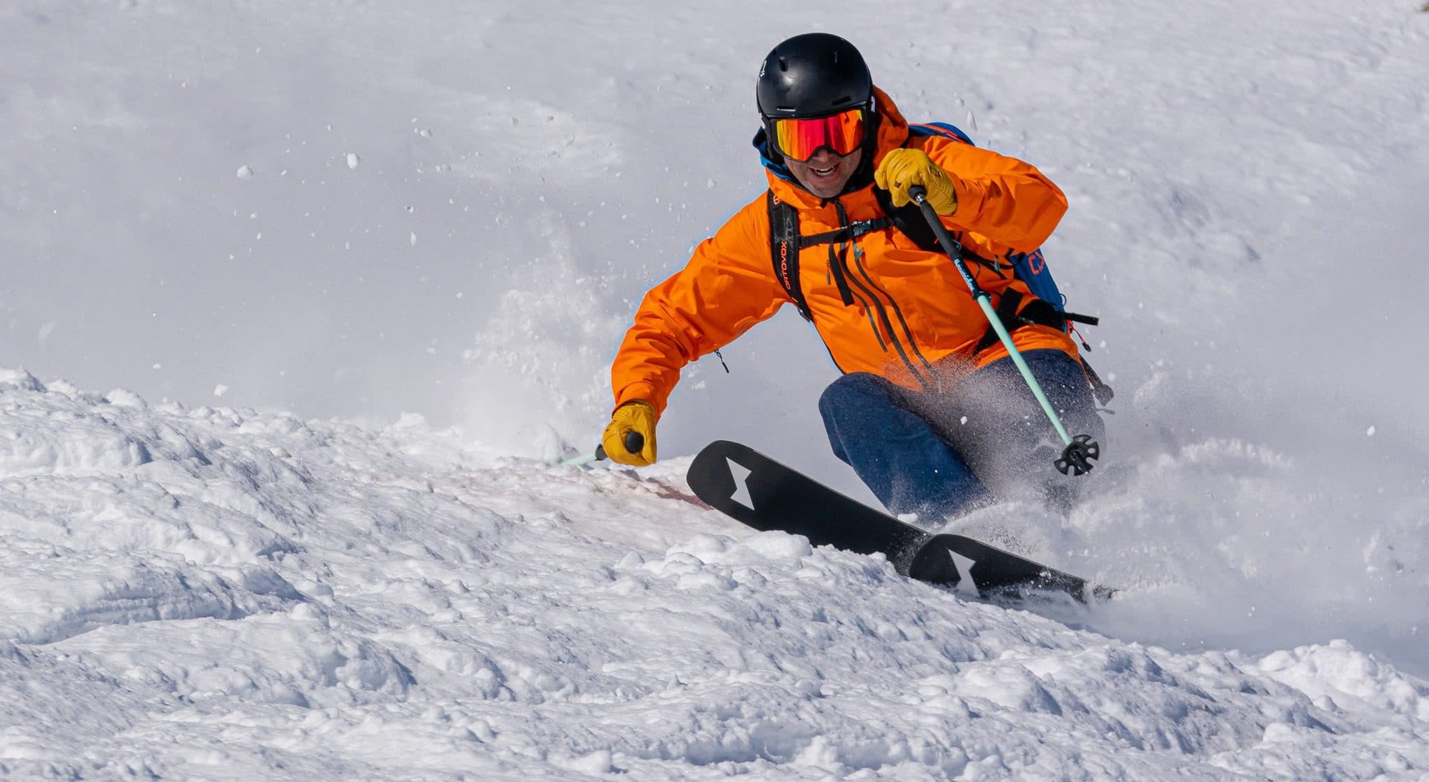 Chris Davenport carving a powder turn in orange jacket